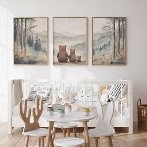 May include: Three framed watercolour prints showing a forest scene with a bear family, and a cot with decorative pillows. The prints have a soft colour palette of greens, browns, and blues. A small white table and chairs are in front of the cot.