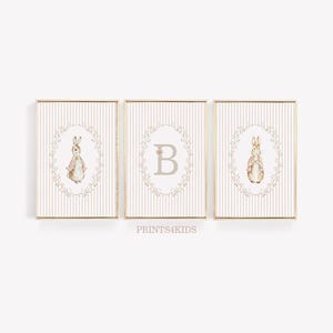 Pode incluir: Três quadros decorativos com fundo de riscas verticais bege e brancas. Os quadros exteriores apresentam um coelho em aguarela dentro de uma coroa de flores, enquanto o central exibe a letra B dentro de uma coroa de flores.