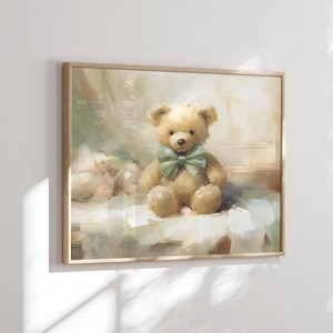 May include: A framed print of a watercolor painting featuring a tan teddy bear with a green bow tie. The bear sits on a white surface with a soft, blurred background. The frame is made of light-colored wood.