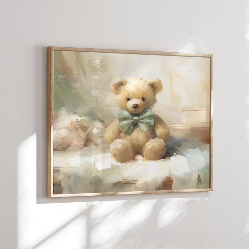 May include: A framed print of a watercolor painting featuring a tan teddy bear with a green bow tie. The bear sits on a white surface with a soft, blurred background. The frame is made of light-colored wood.