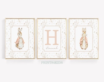 May include: Three framed prints with a white background and gold trim. The center print features a large pink letter H with the name Hannah below it. The prints on either side feature a watercolor illustration of a brown rabbit wearing a pink jacket.
