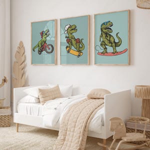 Puede incluir: Tres ilustraciones enmarcadas de dinosaurios en patinetas y bicicletas. Los dinosaurios son verdes y tienen diferentes expresiones. Los marcos son de madera clara y tienen un fondo azul claro.