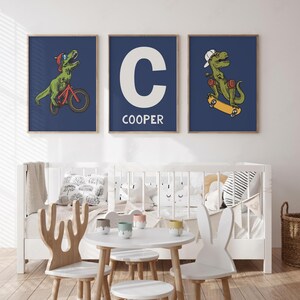 May include: Three blue framed prints with illustrations of a dinosaur riding a bicycle, a dinosaur skateboarding, and a white letter C with the name "COOPER" below it.