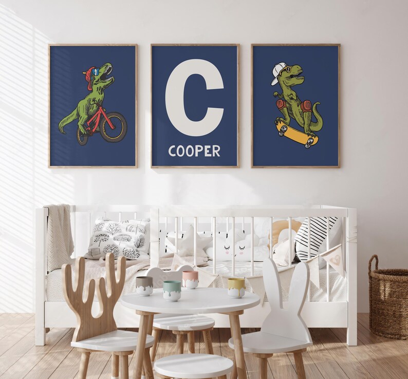 May include: Three blue framed prints with illustrations of a dinosaur riding a bicycle, a dinosaur skateboarding, and a white letter C with the name "COOPER" below it.