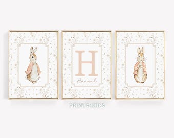 Könnte beinhalten: Drei gerahmte Drucke mit weißem Hintergrund und goldener Umrandung. Der mittlere Druck zeigt einen großen rosa Buchstaben H mit dem Namen Hannah darunter. Die Drucke auf beiden Seiten zeigen eine Aquarellillustration eines braunen Kaninchens, das eine rosa Jacke trägt.