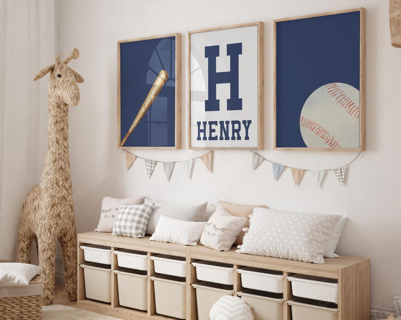 K&ouml;nnte beinhalten: Drei gerahmte Drucke mit einem marineblauen Hintergrund. Der erste Druck zeigt einen Baseballschl&auml;ger und einen Ball, der zweite Druck zeigt einen gro&szlig;en wei&szlig;en Buchstaben H mit dem Namen Henry darunter, und der dritte Druck zeigt einen Baseball. Die Drucke h&auml;ngen an einer wei&szlig;en Wand &uuml;ber einer Holzaufbewahrungsbank mit wei&szlig;en Beh&auml;ltern.