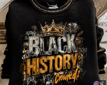 May include: Black sweatshirt with gold trim around the collar. The front features the words "BLACK HISTORY CROWNED" in gold and white, with a gold crown above the words. The design has a graffiti-style aesthetic.