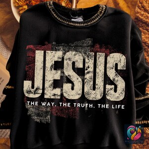 May include: Black sweatshirt with the word "JESUS" in large, distressed white letters. Below, the text reads "THE WAY, THE TRUTH, THE LIFE" in a smaller font. The design includes a red and gray distressed background.