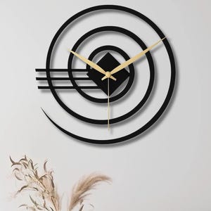 May include: A modern black wall clock with a geometric design. The clock features concentric circles, a square center, and gold-colored hands. The clock is mounted on a white wall, adding a contemporary touch to the room's decor.