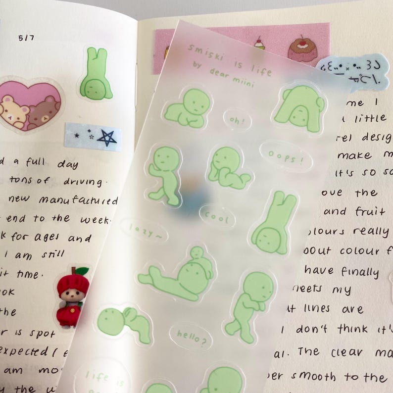 May include: A sheet of clear stickers featuring green cartoon figures in a variety of poses. The stickers are labelled with phrases such as "cool", "oops", "hello?" and "smiski is life by dear miini".