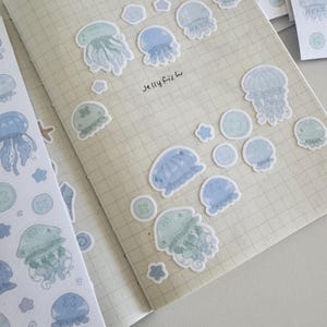 May include: A sheet of blue and green watercolor stickers featuring jellyfish, stars, and buttons. The text "Jellyfish" is written in cursive on the sheet.