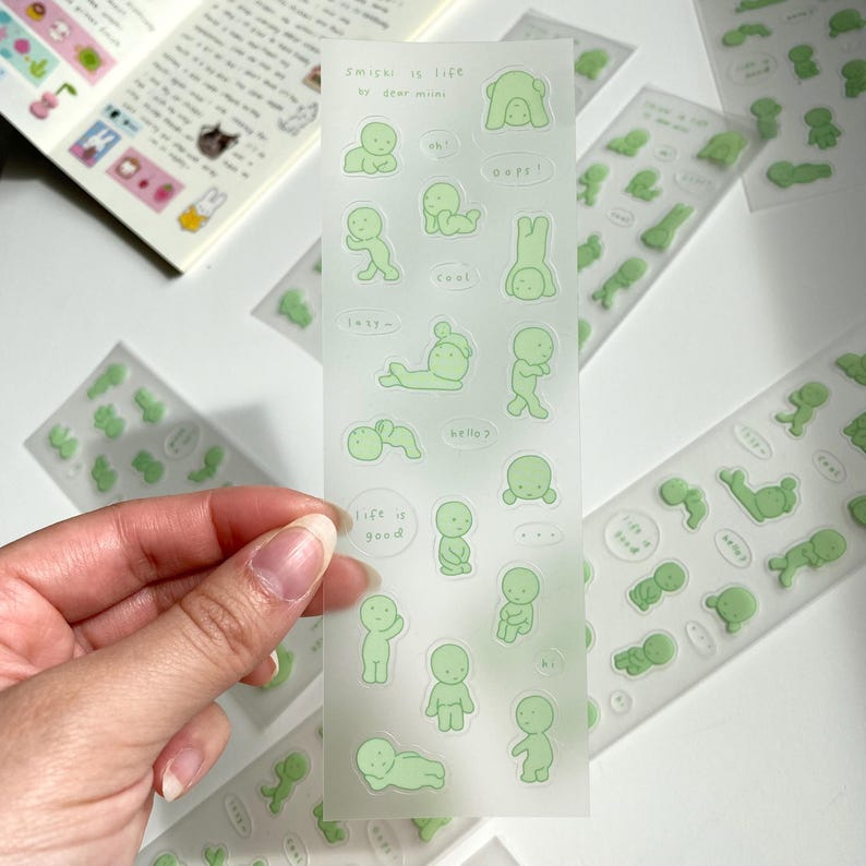 May include: A sheet of clear stickers with green illustrations of stick figures in various poses. The stickers feature phrases like "life is good", "hello", "cool", and "lazy".