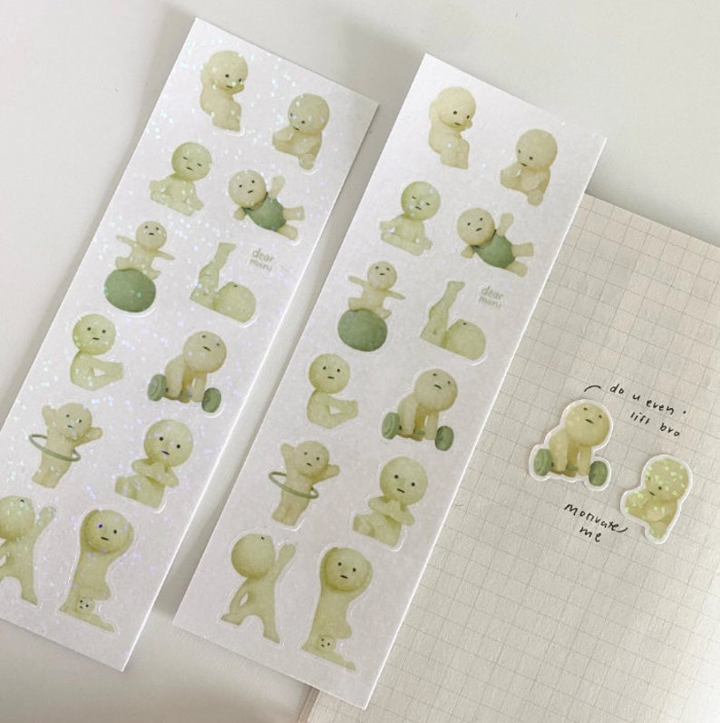 May include: Two sheets of stickers featuring illustrations of cartoon characters doing various exercises. The characters are light green and have a simple design. The stickers are on a white background with a subtle glitter effect. The text on the stickers reads "Dear Mom!"