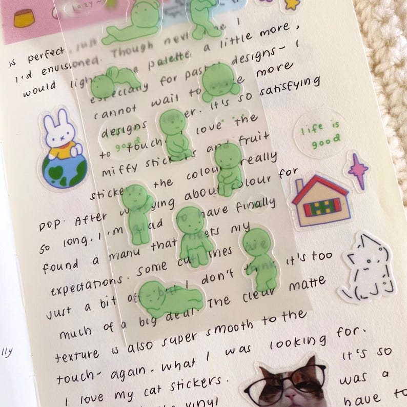 May include: A collection of colourful stickers featuring a variety of designs, including a bunny holding a globe, a house, a cat wearing glasses, and several green figures. The stickers are on a white background with handwritten text.