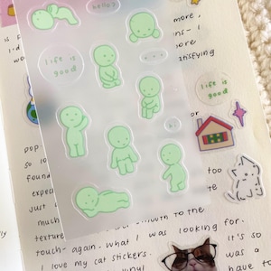 May include: A sheet of clear stickers with green cartoon figures in various poses. The stickers feature the text "life is good" and "hello?"