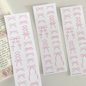 May include: Three sheets of pink and white sticker paper with various pink ribbon designs. The stickers feature bows, criss-cross ribbons, and other ribbon designs. The sheets are labeled with the text "2023 dear mini".