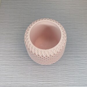 May include: A pink ceramic planter with a textured, geometric design. The planter is empty and has a round shape.