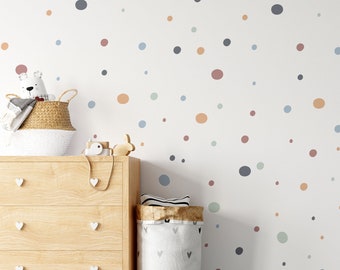 May include: A white wall with a colorful polka dot pattern in shades of blue, orange, and brown. The wall is decorated with a wooden dresser with three drawers and a white ceramic toy bear.