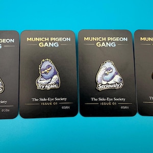 Könnte beinhalten: Vier Emaille-Anstecknadeln auf schwarzen Karten mit einem Cartoon-Tauben-Design. Die Anstecknadeln tragen die Aufschrift "Munich Pigeon Gang" und "The Side-Eye Society". Slogans sind "Try Thinking", "Try again", "Seriously?" und "Go on."