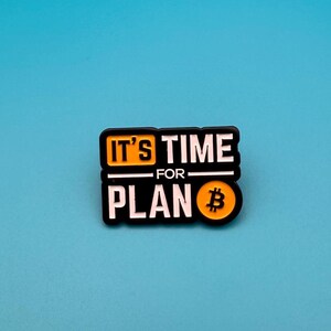 Puede incluir: Un pin negro y amarillo con el texto "IT'S TIME FOR PLAN" en letras blancas. El símbolo de Bitcoin está en la parte inferior derecha. El pin está sobre un fondo azul liso.