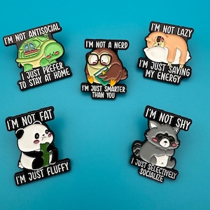 May include: A collection of five cartoon character pins with humorous phrases. The pins feature a turtle, owl, sloth, panda, and raccoon. Each pin has a black border and a unique saying, such as "I'm not antisocial, I just prefer to stay at home."