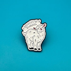 Könnte beinhalten: Ein weißer Emaille-Pin mit einem Cartoon-Lama und dem Text "I Identify as a Problem". Das Lama hat einen schwarzen Umriss, rosa Ohren und einen verspielten Ausdruck. Der Pin ist vor einem helltürkisen Hintergrund platziert.