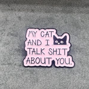 Könnte beinhalten: Rosa emaillierte Anstecknadel mit schwarzem Umriss, die eine schwarze Katze zeigt, die über den Rand schaut, und den Text "My cat and I talk shit about you."