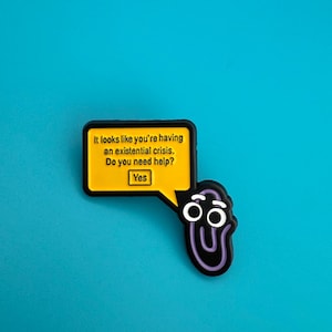 Peut inclure: Un charm en forme de trombone noir et violet avec une bulle de dialogue jaune. La bulle de dialogue contient le texte : "It looks like you're having an existential crisis. Do you need help? Yes" sur fond bleu.