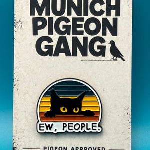 Könnte beinhalten: Anstecknadel mit einer schwarzen Katze mit gelben Augen, vor einem Sonnenuntergangsdesign, mit dem Text "EW, PEOPLE". Die Anstecknadel befindet sich auf einer Karte mit "MUNICH PIGEON GANG" und "PIGEON APPROVED".