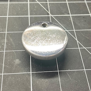 May include: A silver-colored round metal cap with a small hole in the center.