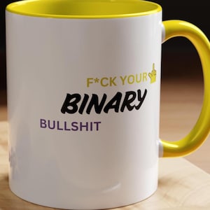Puede incluir: Taza de cerámica blanca con interior y asa amarillos. La taza presenta el texto "F*CK YOUR BINARY BULLSHIT" en letras negras, amarillas y moradas. También se muestra una mano con el dedo medio levantado.