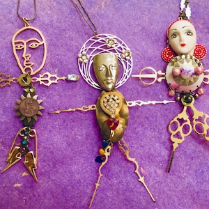 May include: Three gold-toned ornaments with different faces and designs. The ornaments are made of metal and have a variety of embellishments, including beads, rhinestones, and a coin.