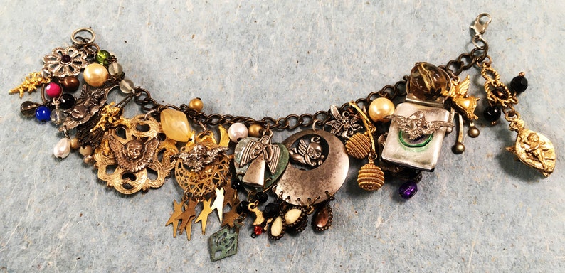 May include: A gold charm bracelet with a variety of charms, including angels, stars, and a crescent moon. The bracelet is made of metal and has a chain link design.