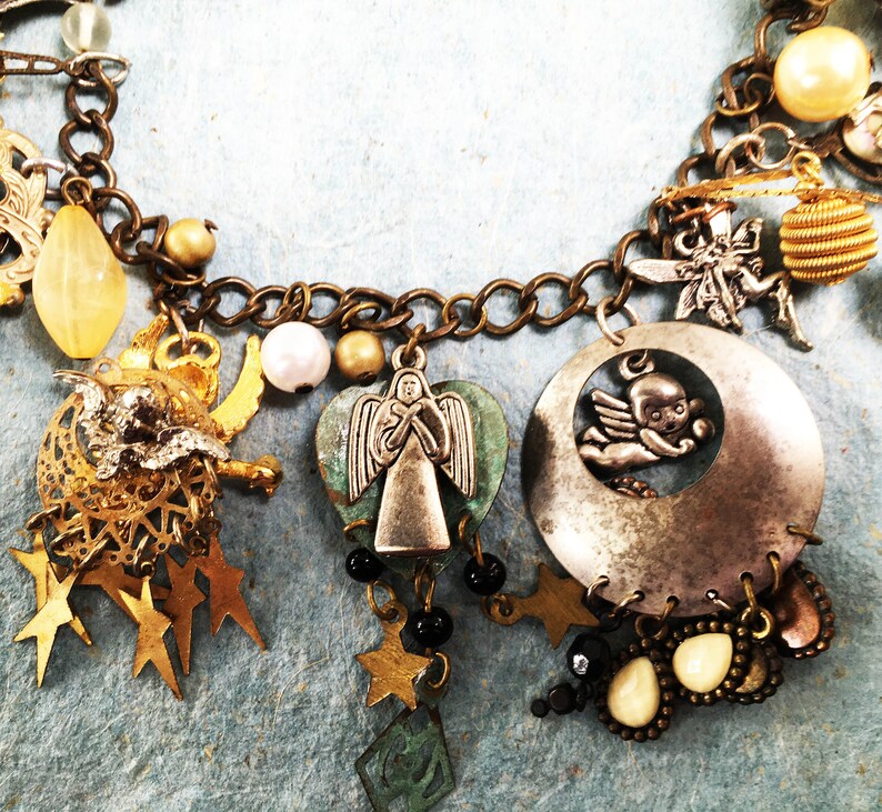 May include: A silver charm bracelet with a variety of charms, including a heart-shaped charm with an angel, a crescent moon charm with a cherub, and a star charm. The bracelet is made of brass and has a silver finish.