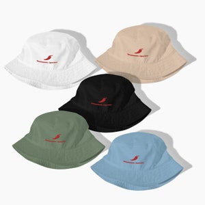 Puede incluir: Cinco sombreros de pescador en diferentes colores: blanco, beige, negro, verde y azul claro. Cada sombrero tiene un gráfico de chile rojo y el texto "Smooth Operator" bordado en la parte delantera.