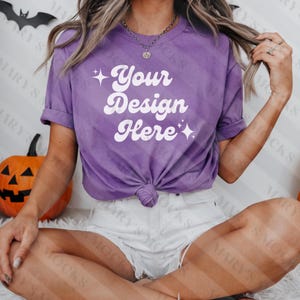 Puede incluir: Una camiseta morada de manga corta y cuello redondo. La camiseta tiene el texto "Your Design Here" en una fuente retro.
