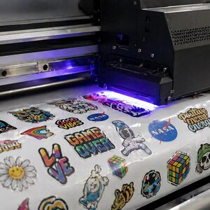 A close-up view of a sticker printer in operation, with various colorful stickers being printed on a roll of paper.