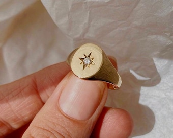 May include: A gold signet ring with a star design and a small clear stone in the center.