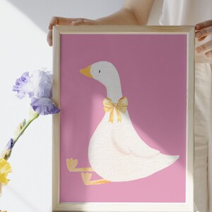 May include: A framed print of a white goose with a yellow bow sitting on a pink background.