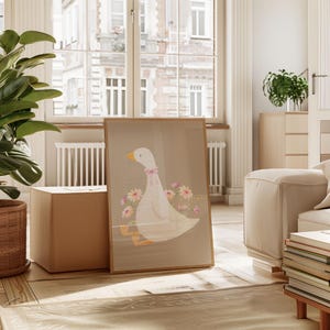 May include: A framed illustration of a white goose with a pink bow sitting on a brown background with pink flowers. The goose is surrounded by pink flowers.