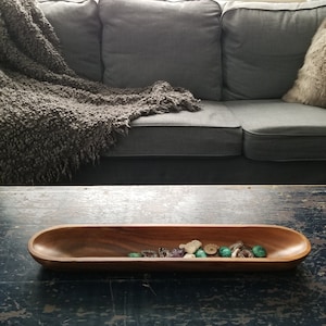 May include: A long, wooden serving bowl filled with a variety of small, colourful stones. The bowl is sitting on a dark wooden table.