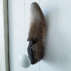 May include: A wooden shoe last with a white porcelain door knob attached to it. The shoe last is brown and has the letters "7 EA" carved into it. The door knob is attached to the shoe last with a metal bracket.