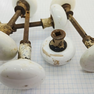 Peut inclure: Ensemble de poignées de porte anciennes en porcelaine blanche avec des ferrures métalliques rouillées et vieillies. Les boutons sont ovales et présentent des signes d'usure, suggérant qu'il s'agit d'articles vintage ou récupérés.