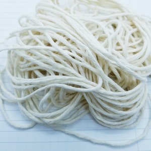 May include: A close-up of a pile of white cotton twine. The twine is tightly wound and appears to be natural and unbleached.