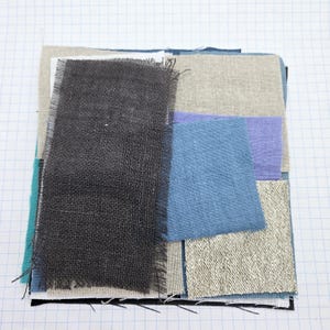 May include: A collection of fabric swatches in various shades of blue, grey, and beige. The swatches are arranged in a grid pattern and have a rough, textured surface.