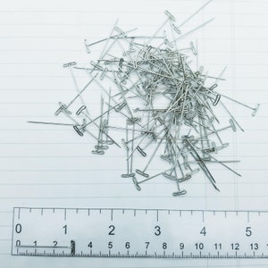 May include: A pile of silver T-pins on a white surface with a ruler marked in inches. The ruler is labelled with numbers from 0 to 5.