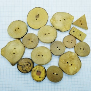 May include: A collection of 15 wooden buttons in various shapes and sizes. The buttons are made of natural wood and have a rustic, handmade look. Some buttons are round, some are oval, and some are shaped like triangles. The buttons are all different sizes, ranging from about 2.5 cm to 5 cm in diameter.