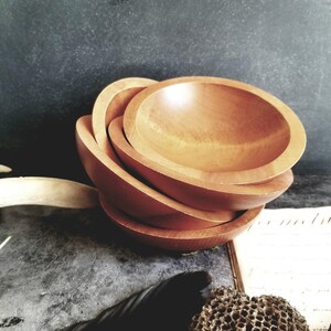 May include: Set of four wooden bowls, nested together. The bowls are a light brown colour and have a smooth, polished finish.