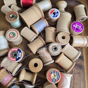 May include: A collection of wooden spools of thread in various colours and sizes. The spools are labelled with different brands and thread types, including "J&P Coats", "National", "Peerless", and "Drima".
