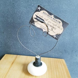 May include: A white ceramic knob with a black metal base and a wire heart-shaped frame holding a business card. The business card reads "Brenda Braun, I make stuff you might like it. Instagram @DECADENCE2, cadence2@hotmail.com, DECADENCEZ.com"